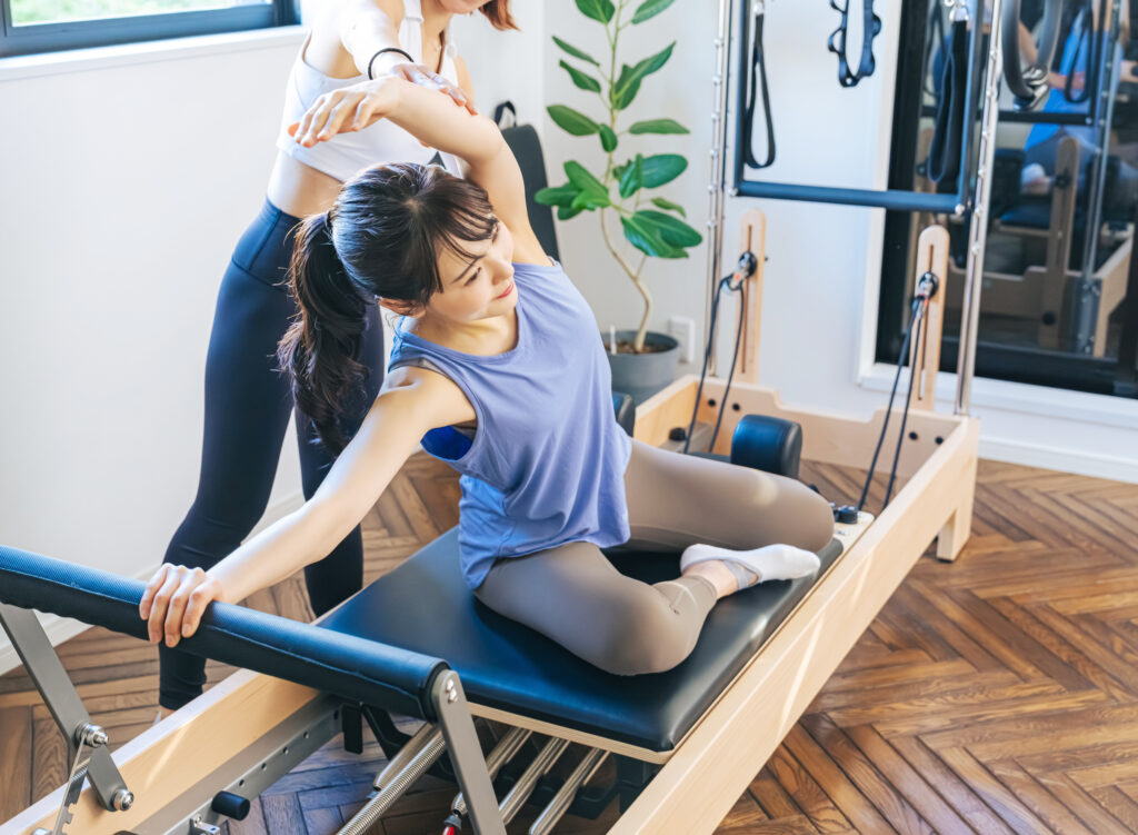 ピラティススタジオでインストラクターからマシンピラティスのレッスンを受ける女性