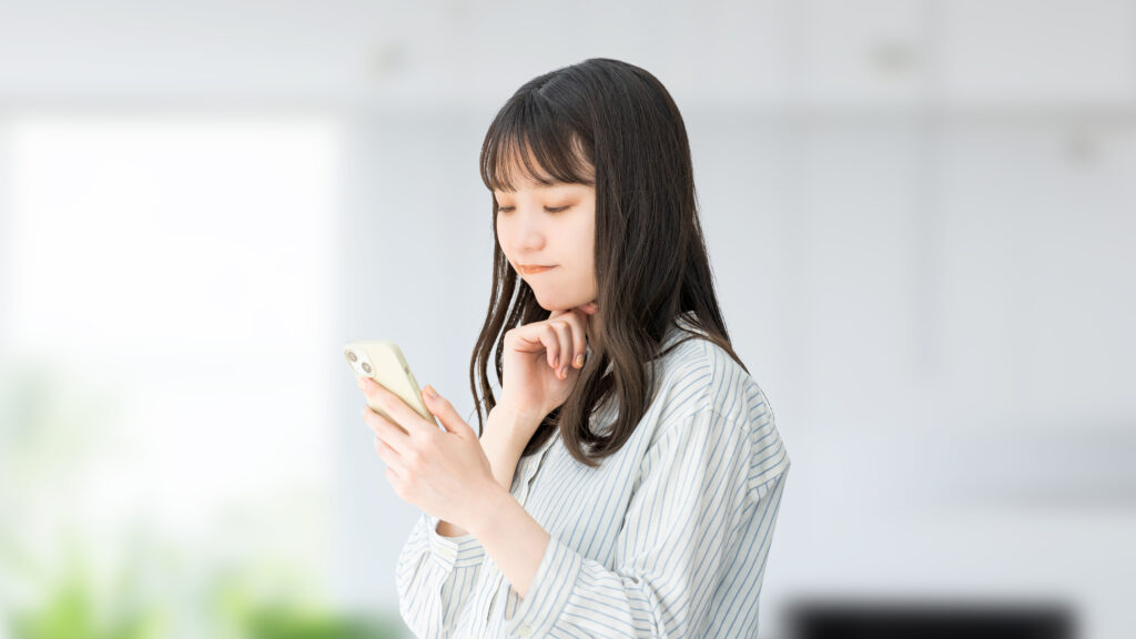 スマホを見て考える若い日本人女性・ビジネスウーマン