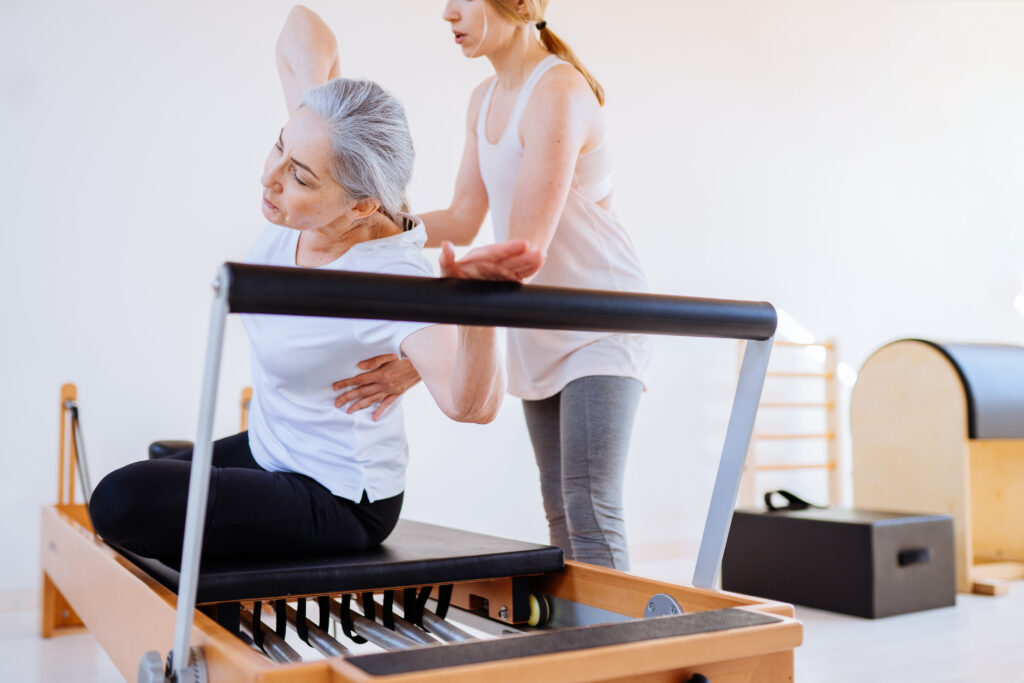 パーソナルトレーナーがジムでマシンを使って運動する年配の女性を指導する