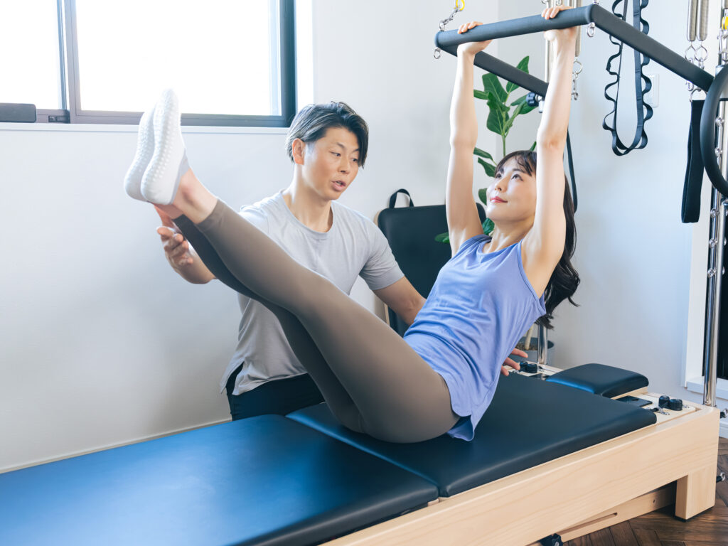 ピラティススタジオでインストラクターからマシンピラティスのレッスンを受ける女性