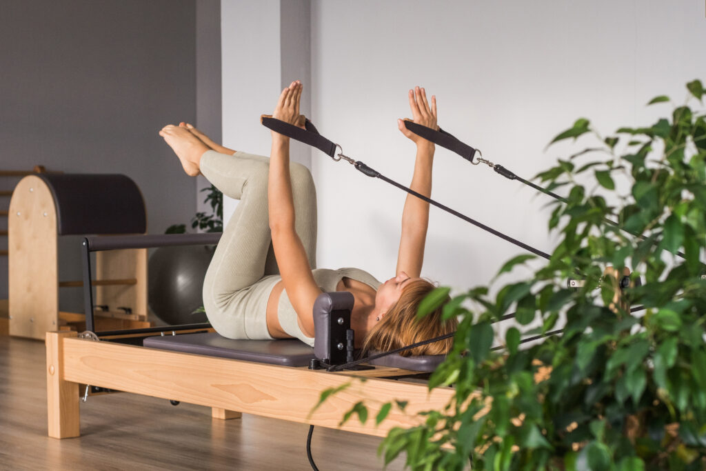 リフォーマーベッドでピラティスのトレーニングをする女性。