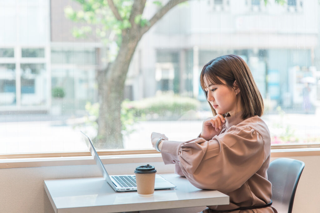 カフェでパソコンを使いながら腕時計を確認する日本人ビジネスウーマン