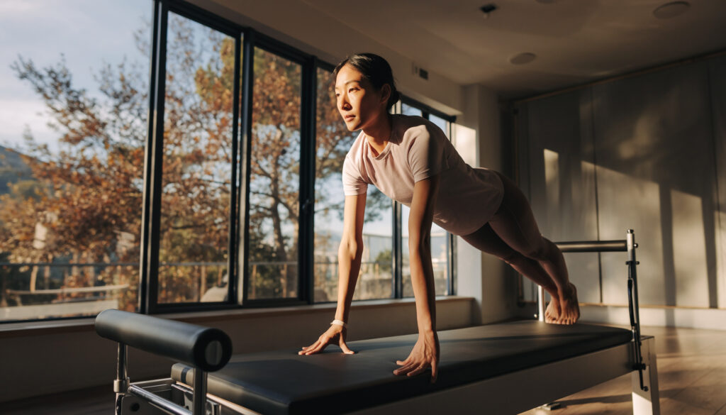 窓からクスノキが見えるピラティススタジオでピラティスをする日本人女性