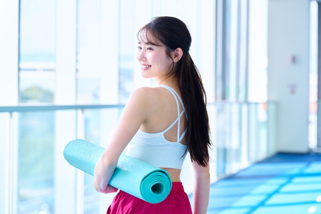 ヨガマットを持って振り返る笑顔の若い女性